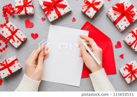 top view photo of valentine day decor female hands holding letter with envelope, small gift box and heart decoration on isolated pastel colored background with empty space top view photo of valentine day decor female hands holding letter with envelope, small gift box and heart decoration on isolated pastel colored background with empty space 115658531