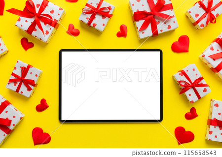 Top view of digital tablet with gift boxes and hearts on colorful background. Tablet with black screen with Holiday decorations gift box top view 115658543