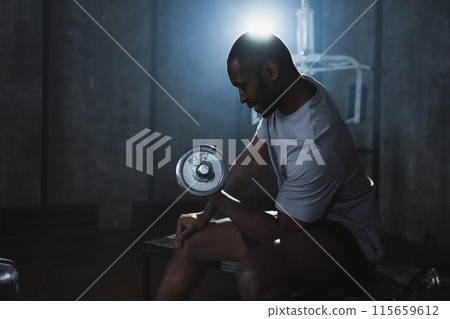 Fitness workout in gym. African American man bodybuilder picking up dumbbells in gym. Workout weight training biceps muscles with dumbbell in fitness club. Man doing sports exercise. Healthy lifestyle Fitness workout in gym. African American man bodybuilder picking up dumbbells in gym. Workout weight training biceps muscles with dumbbell in fitness club. Man doing sports exercise. Healthy lifestyle 115659612