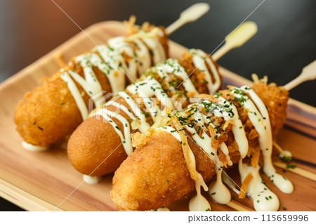 Crispy corn dogs with creamy mayo and sesame seeds on a wooden tray 115659996