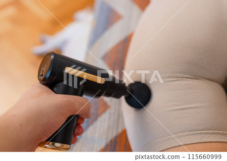 Gun shock vibration percussion massage therapy. Sporty woman practicing self-massaging your legs close up. Applying therapeutic percussive massage gun in living room at home indoors. Copy text space Gun shock vibration percussion massage therapy. Sporty woman practicing self-massaging your legs close up. Applying therapeutic percussive massage gun in living room at home indoors. Copy text space 115660999