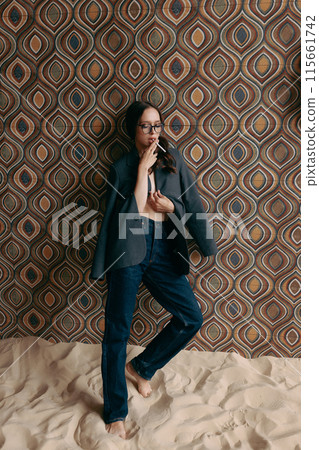Woman in an unbuttoned jacket and jeans posing against a wall 115661742