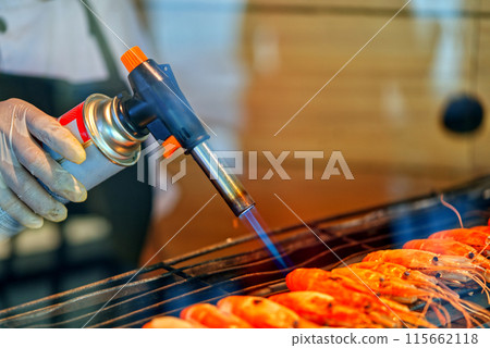 Close up hand with rubber glove holding hand held food burner burning shrimps, space for copy and design, landscape image. Close up hand with rubber glove holding hand held food burner burning shrimps, space for copy and design, landscape image. 115662118