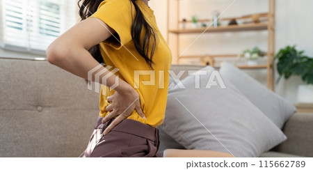Woman experiencing back pain at home. Concept of physical discomfort Woman experiencing back pain at home. Concept of physical discomfort 115662789