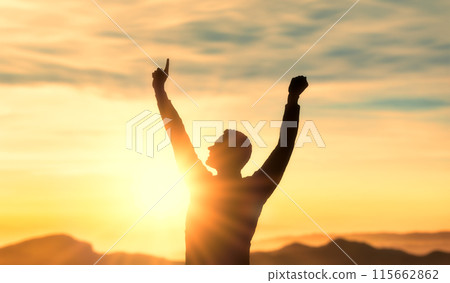 Success, achieving goals in business and life, feeling of triumph. , symbol of achievement. silhouette of man on top of mountain with his arms raised in triumph at sunset, joy and satisfaction 115662862