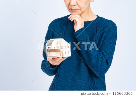 一位擔心的高級女性拿著房屋模型 115663305