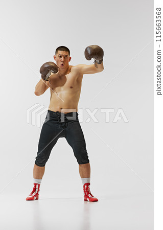 Shirtless emotional young man, young boxer training hard, captured mid-punch pose isolated on white background. 115663568