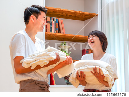 一對夫婦一邊搬運衣物一邊微笑著交談 115663576