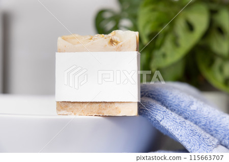 Soap bar with blank label on vessel sink near blue towels and plant close up, mockup 115663707