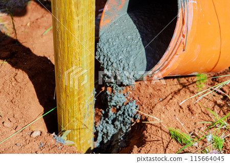 Pouring concrete over newly installed timber fencing wooden fence posts 115664045