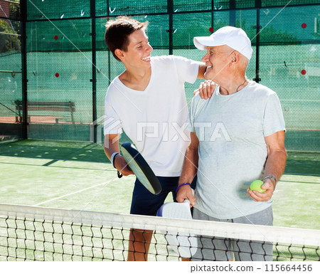 Older man and a young man talking on court playing paddle Older man and a young man talking on court playing paddle 115664456