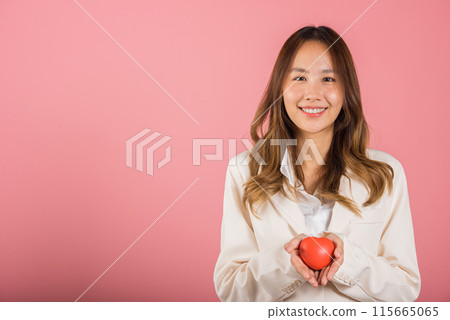 Smiling woman confidence showing holding red heart with her hand palm isolated pink background, Asian happy portrait beautiful young female send love and happy valentine in studio shot, copy space 115665065