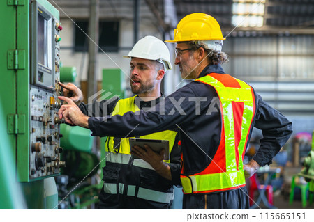 Two men in safety gear are working on a machine 115665151