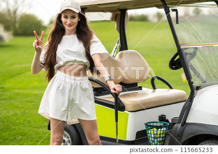 Beautiful golfer posing by the vehicle with golf equipment on the green 115665233