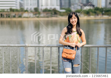 Sky, water, and smile a positive lady in an orange shirt enjoys a sunny day by the lake, a perfect vacation. 115665461