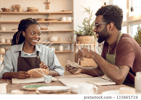 African american male sculptor explaining something to a female student in a pottery workshop African american male sculptor explaining something to a female student in a pottery workshop 115665719