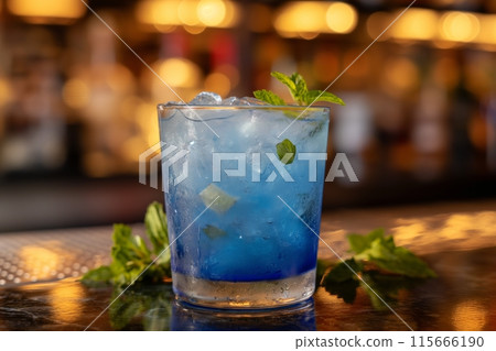A cool blue Mojito in a short glass topped with mint leaves on a bar counter with bokeh background 115666190