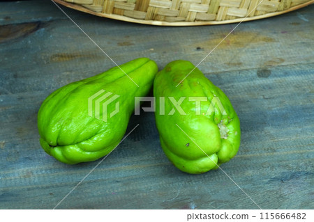 two chayotes, a type of squash, on a wooden table. two chayotes, a type of squash, on a wooden table. 115666482