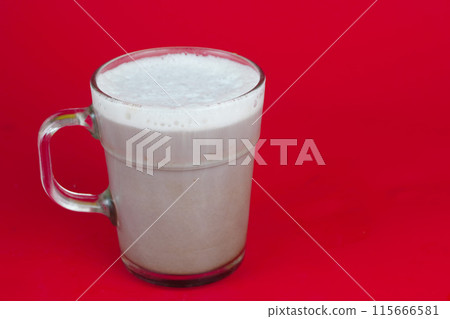 A glass of chocolate milk with a sheen sits on a red background. A glass of chocolate milk with a sheen sits on a red background. 115666581