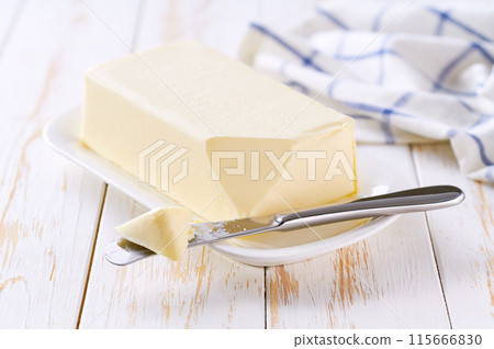 Piece of fresh butter on white plate with knife. White table and shallow focus Piece of fresh butter on white plate with knife. White table and shallow focus 115666830