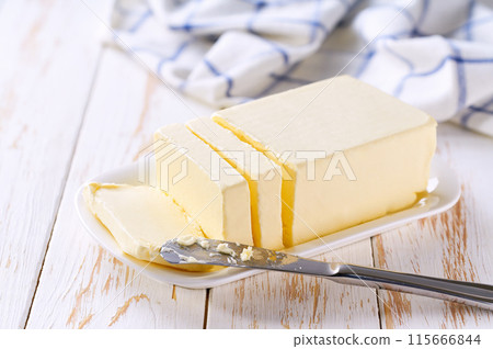 piece of butter in a white ceramic butter dish on a light table. 115666844