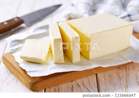 cut block butter on a whitw wooden table, selective focus. Stick of butter, cut. 115666847
