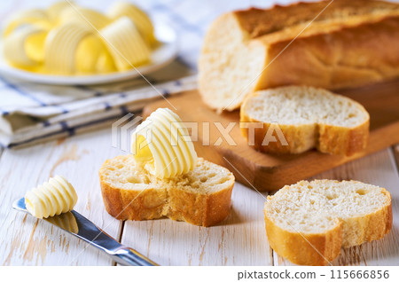 Sliced baguette with butter on a white wooden table. 115666856