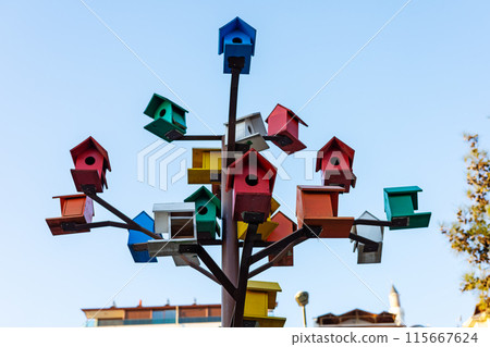 Vibrant birdhouses perched on a metal tree against the sky. 115667624