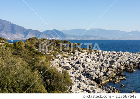 Rocky shoreline framed by mountainous backdrop Rocky shoreline framed by mountainous backdrop 115667642