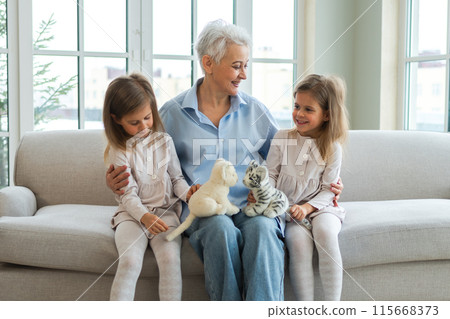 Happy family at home. Two little girls sisters twins grandmother enjoying time together. Good time at home. Grandma granddaughters child kids playing toys hugging together. Family generations Happy family at home. Two little girls sisters twins grandmother enjoying time together. Good time at home. Grandma granddaughters child kids playing toys hugging together. Family generations 115668373