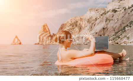 Woman freelancer works on laptop swimming in sea on pink inflatable ring. Happy tourist in sunglasses floating on inflatable donut and working on laptop computer in calm ocean. Remote working anywhere Woman freelancer works on laptop swimming in sea on pink inflatable ring. Happy tourist in sunglasses floating on inflatable donut and working on laptop computer in calm ocean. Remote working anywhere 115668477