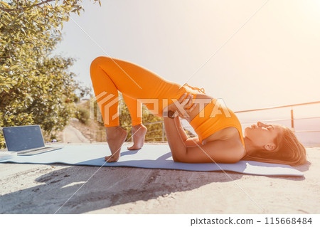 Fitness woman sea. Happy middle aged woman in orange sportswear exercises morning outdoors on yoga mat with laptop in park over ocean beach. Female fitness pilates yoga routine. Healthy lifestyle. Fitness woman sea. Happy middle aged woman in orange sportswear exercises morning outdoors on yoga mat with laptop in park over ocean beach. Female fitness pilates yoga routine. Healthy lifestyle. 115668484