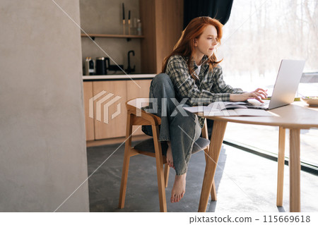 Vertical shot of young business woman reading something in book and typing on laptop keyboard sitting at desk. Female student studying at table with computer and book. Freelancer working on project. Vertical shot of young business woman reading something in book and typing on laptop keyboard sitting at desk. Female student studying at table with computer and book. Freelancer working on project. 115669618