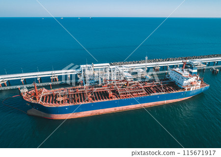 Aerial view of a large oil tanker docked at a pier in the port in process of loading. 115671917