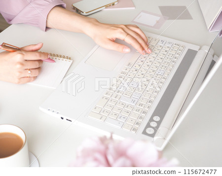 一位女性在辦公桌上使用電腦時記筆記的手，這是一位可愛女性的工作空間 115672477