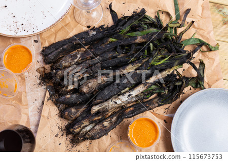 On wooden table covered with paper, fried Catalan green onion kalsot and two small balls of sauce On wooden table covered with paper, fried Catalan green onion kalsot and two small balls of sauce 115673753