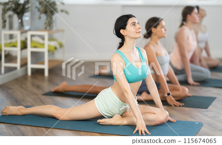 Young girl teaches yoga lesson, shows students technique of performing kapotasana asana 115674065