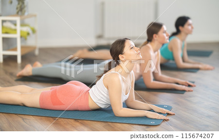 Young girl teaches yoga lesson, shows students technique of performing Urdhva Mukha Shvanasana asana Young girl teaches yoga lesson, shows students technique of performing Urdhva Mukha Shvanasana asana 115674207