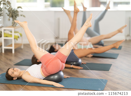 Group of women lying on their backs doing yoga with exercise balls under their backs in studio Group of women lying on their backs doing yoga with exercise balls under their backs in studio 115674213