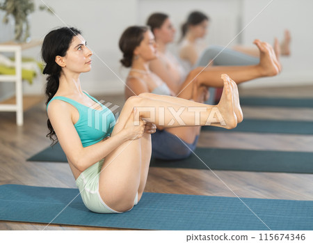 Young women balancing in boat pose Navasana strengthening core muscles and abdominals during daily yoga routine in fitness studio 115674346
