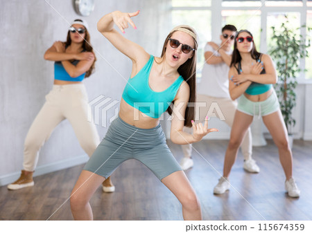 Group of young girls in dark glasses and ball cap and guy dance jazz-funk in fitness club. Group of young girls in dark glasses and ball cap and guy dance jazz-funk in fitness club. 115674359