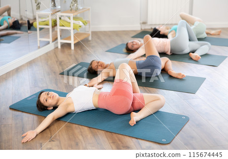Group of women doing different yoga exercises lying on their back in studio Group of women doing different yoga exercises lying on their back in studio 115674445