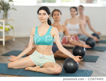 Teacher explains principle of performing body tilts and rests her hand on fitball 115674483