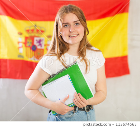 Happy smiling teen girl holding spiral notepads under her arm against of national flag of Spain Happy smiling teen girl holding spiral notepads under her arm against of national flag of Spain 115674565