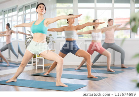 Young girl teaches yoga lesson, shows students technique of performing warrior pose asana 115674699