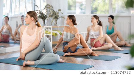Women maintaining mental and physical health attending group yoga class at modern studio, practicing twisting pose Women maintaining mental and physical health attending group yoga class at modern studio, practicing twisting pose 115674752