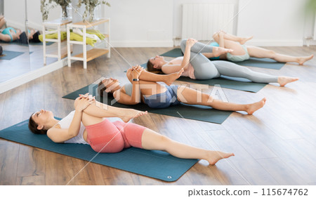 Female students during fitness Pilates training lie on floor on their backs and stretch leg muscles 115674762