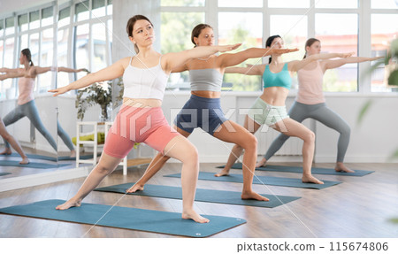 Young girl performing Virabhadrasana asana during group yoga training Young girl performing Virabhadrasana asana during group yoga training 115674806