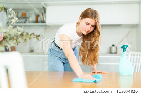 in kitchen,positive housewife in casual clothes holds rag in hands and cleans surface of table in kitchen,positive housewife in casual clothes holds rag in hands and cleans surface of table 115674820