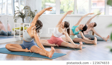 Girl teaches yoga lesson, shows students technique of performing Parivritta Janu Shirshasana asana 115674833